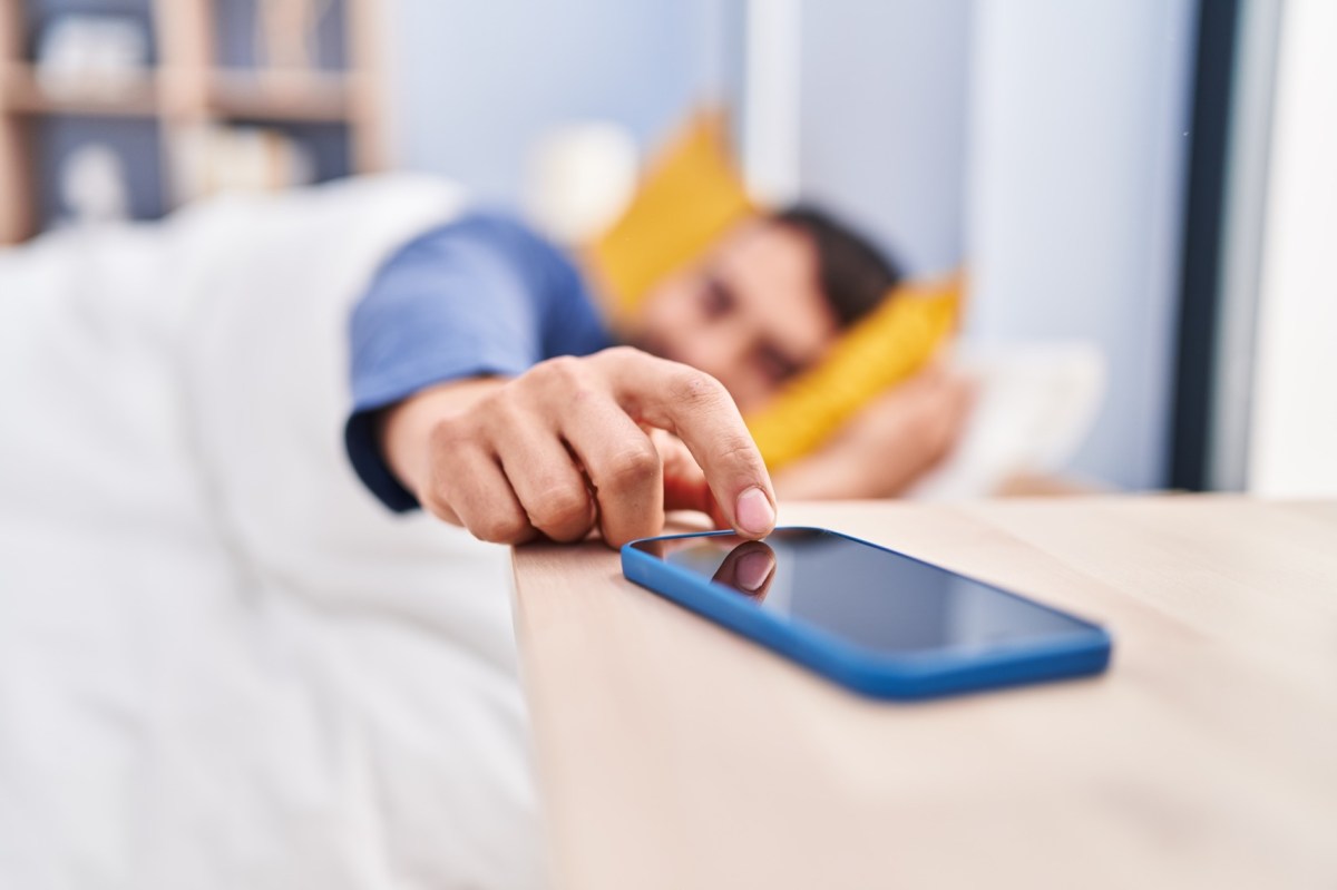 Mann im Bett schaltet sein Handy aus