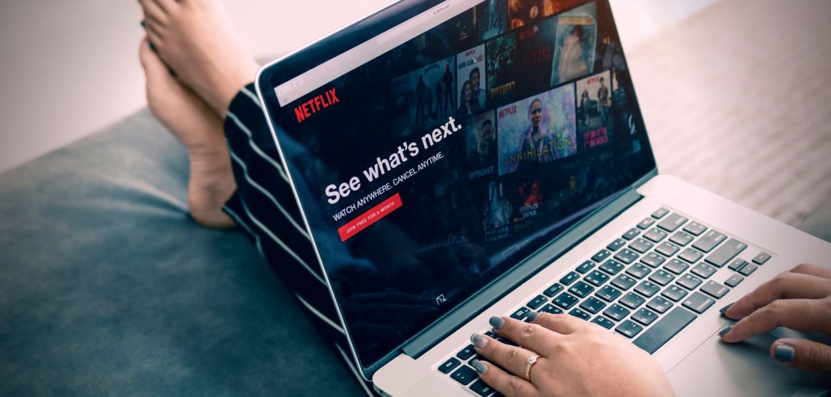Frau sitzt mit Netflix auf dem Laptop auf einem Sofa