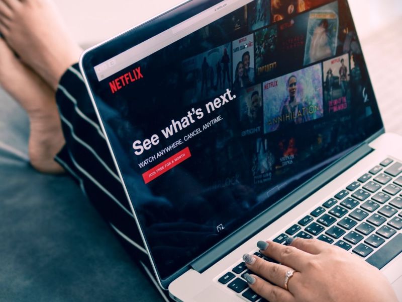 Frau sitzt mit Netflix auf dem Laptop auf einem Sofa