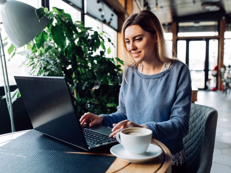 Frau sitzt im Café und tippt auf einem Laptop