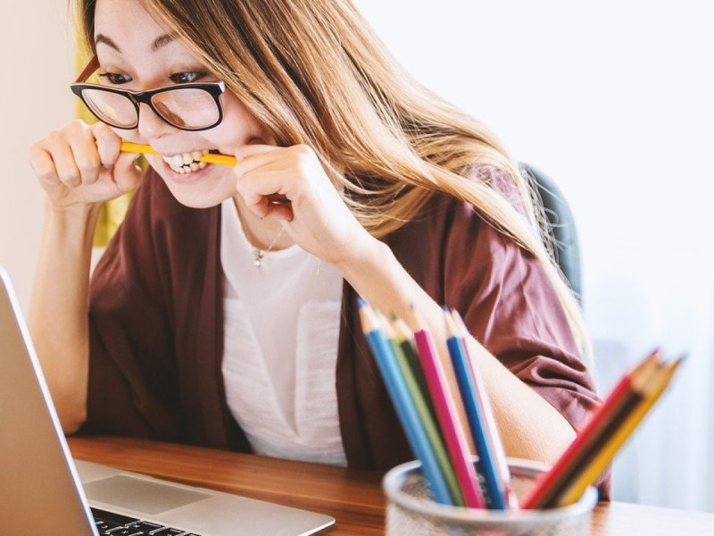 Eine Frau schaut auf ihren Laptop und beißt vor lauter Ärger in ihren Stift.