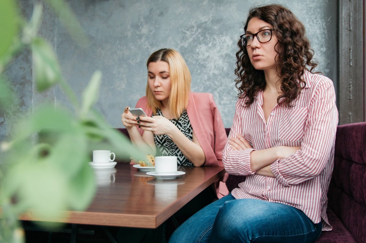 Zwei Frauen sitzen im Café. Eine Frau schaut auf ihr Smartphone