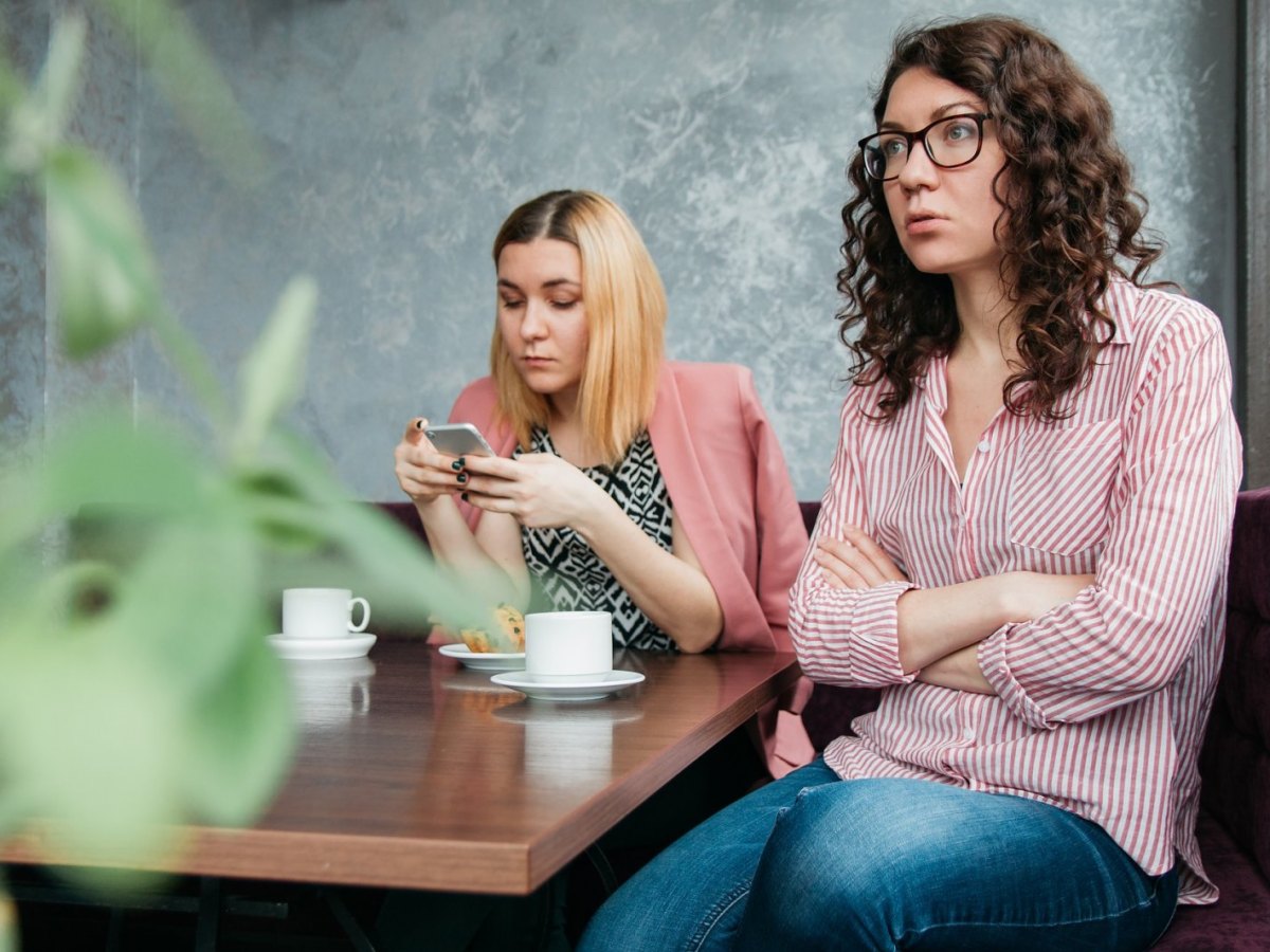 Zwei Frauen sitzen im Café. Eine Frau schaut auf ihr Smartphone