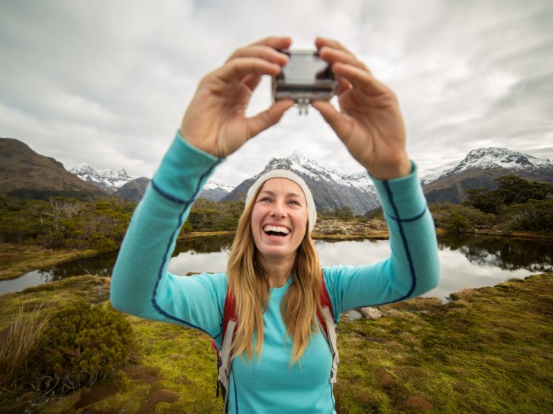 Frau macht in den Bergen ein Selfie mit einer Action-Cam.