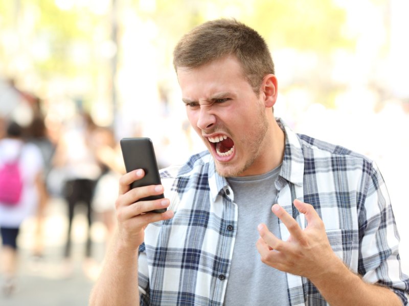 Mann beugt sich wütend übers Handy