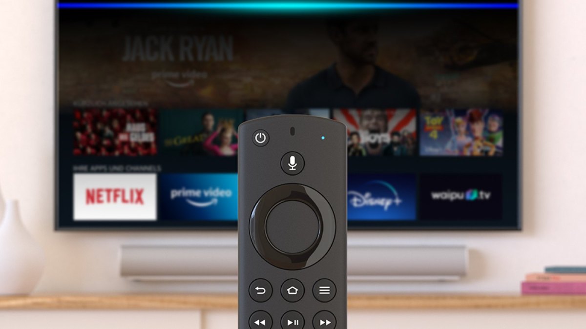 Ein Amazon Fire TV Stick im Vordergrund. Dahinter ein Fernseher mit der Amazon Fire TV-App.