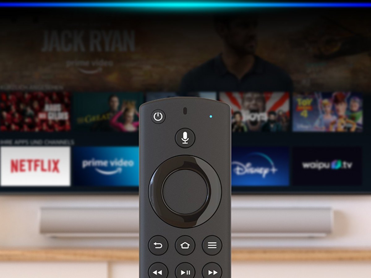 Ein Amazon Fire TV Stick im Vordergrund. Dahinter ein Fernseher mit der Amazon Fire TV-App.