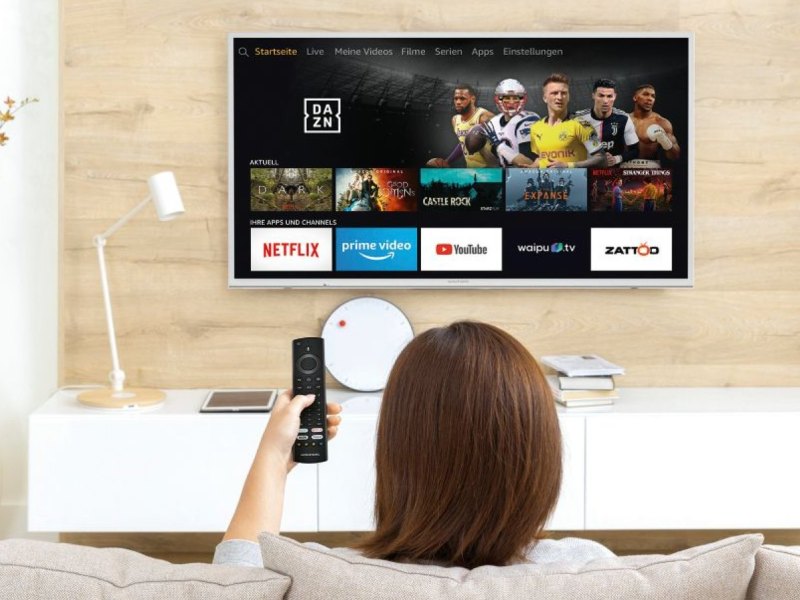 Frau sitzt vorm Fernseher und schaut auf den Amazon Fire TV