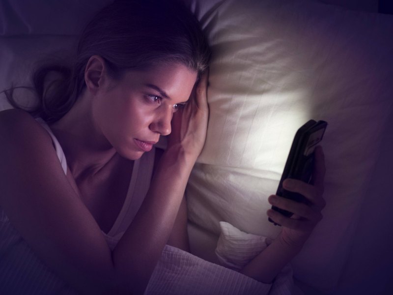 Eine Frau schaut im Dunkeln auf ein leuchtendes Smartphone.-Display.