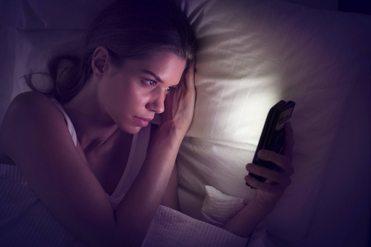 Eine Frau schaut im Dunkeln auf ein leuchtendes Smartphone.-Display.