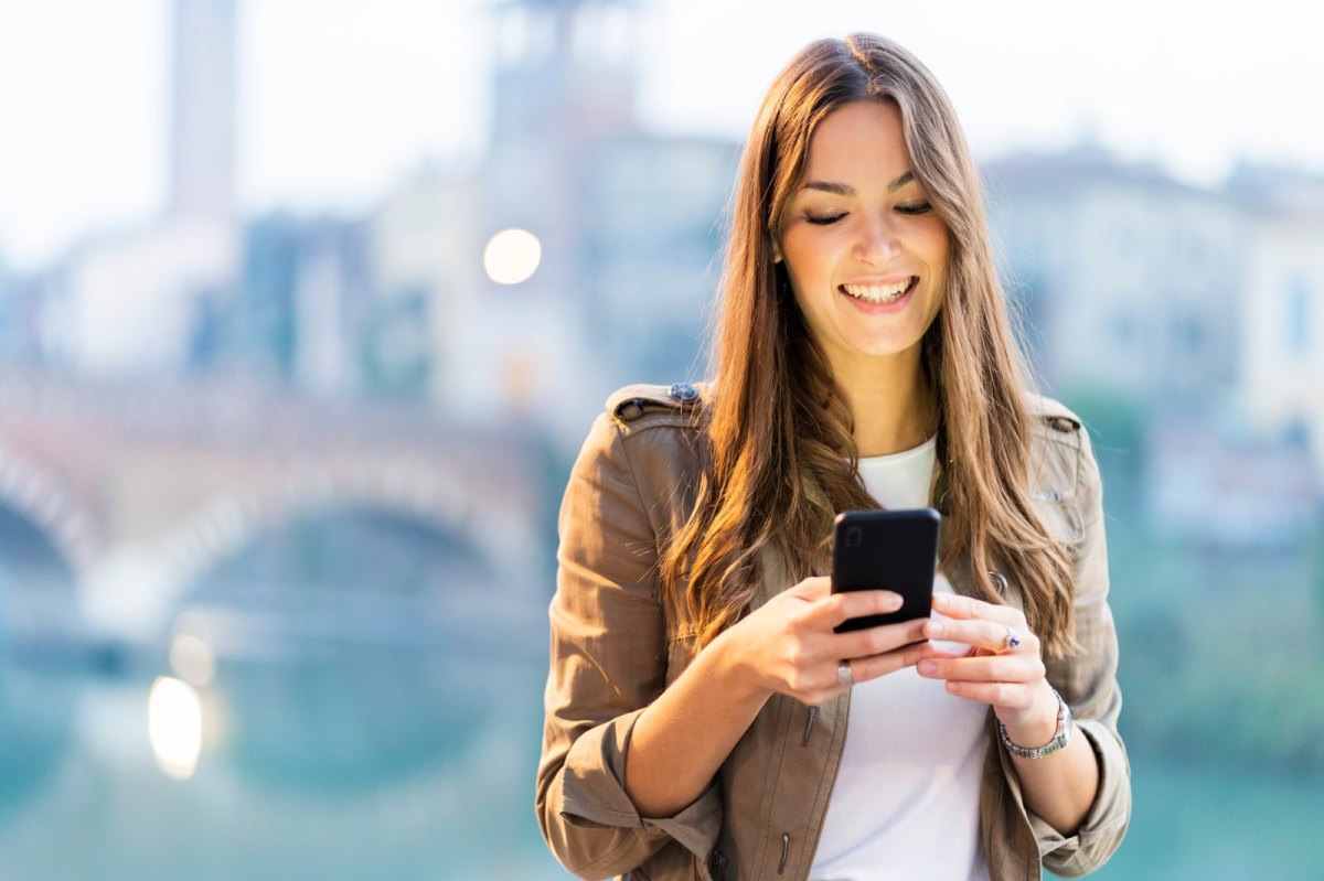 Frau schaut lächelnd auf ihr Handy.