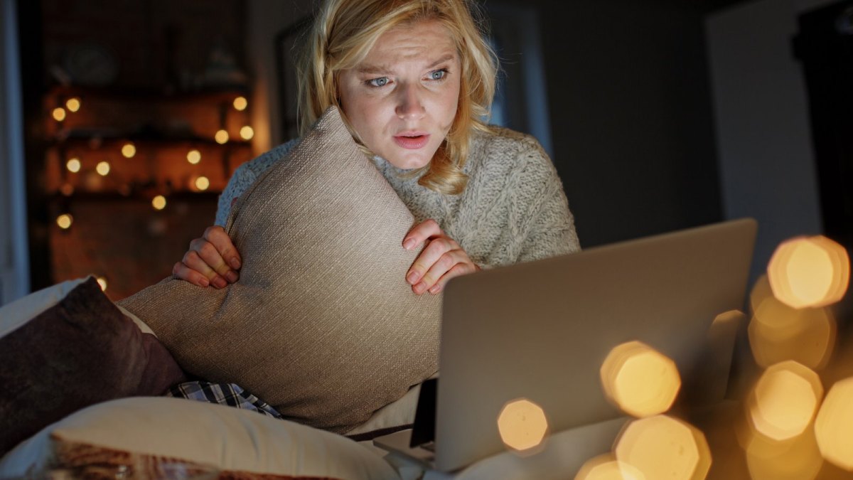 Frau sitzt mit einem Kissen angstvoll vor ihrem Laptop.