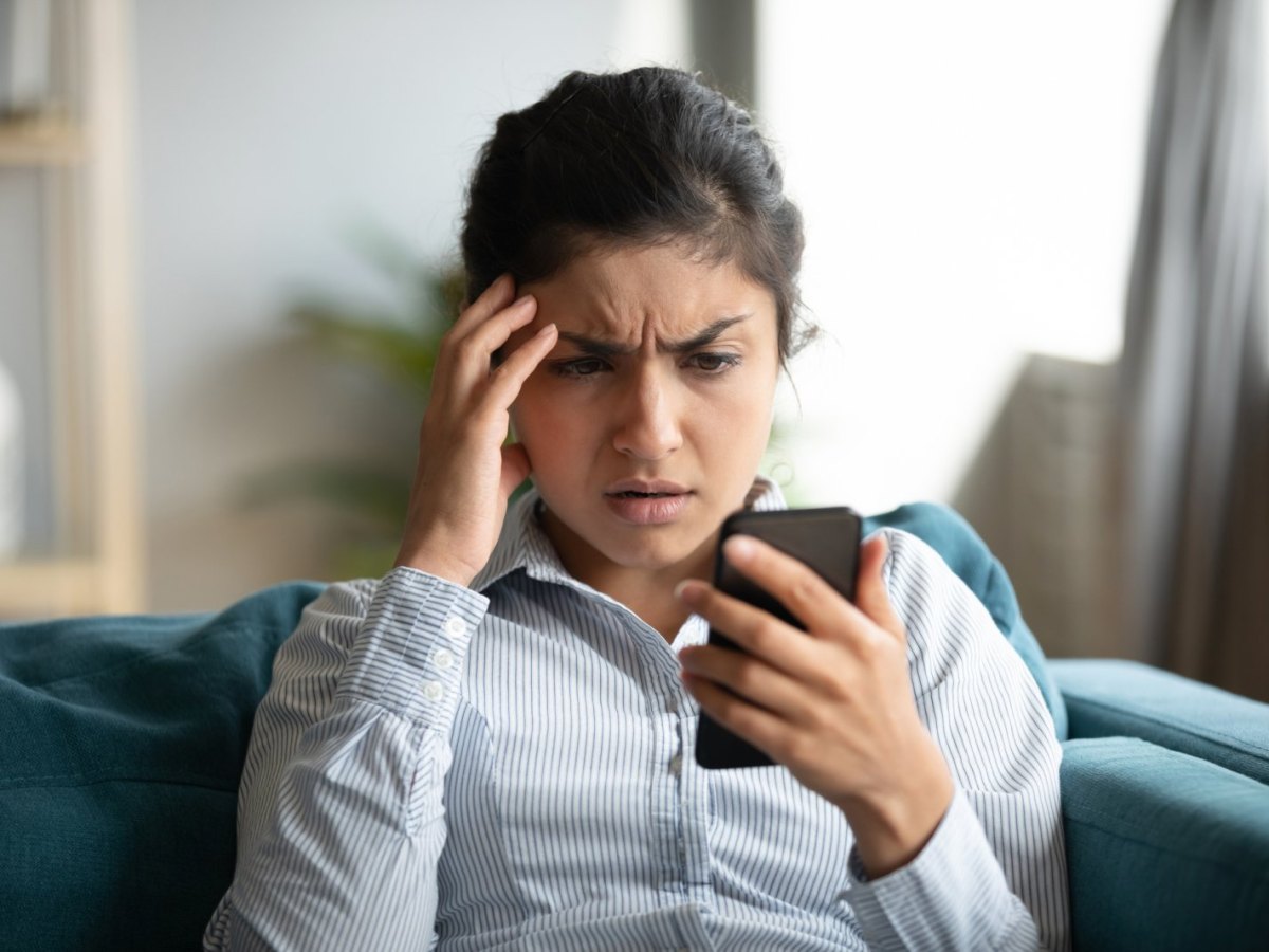 Frau schaut genervt auf ihr Handy.