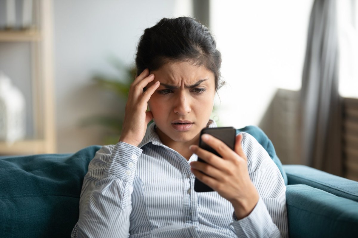 Frau schaut genervt auf ihr Handy.