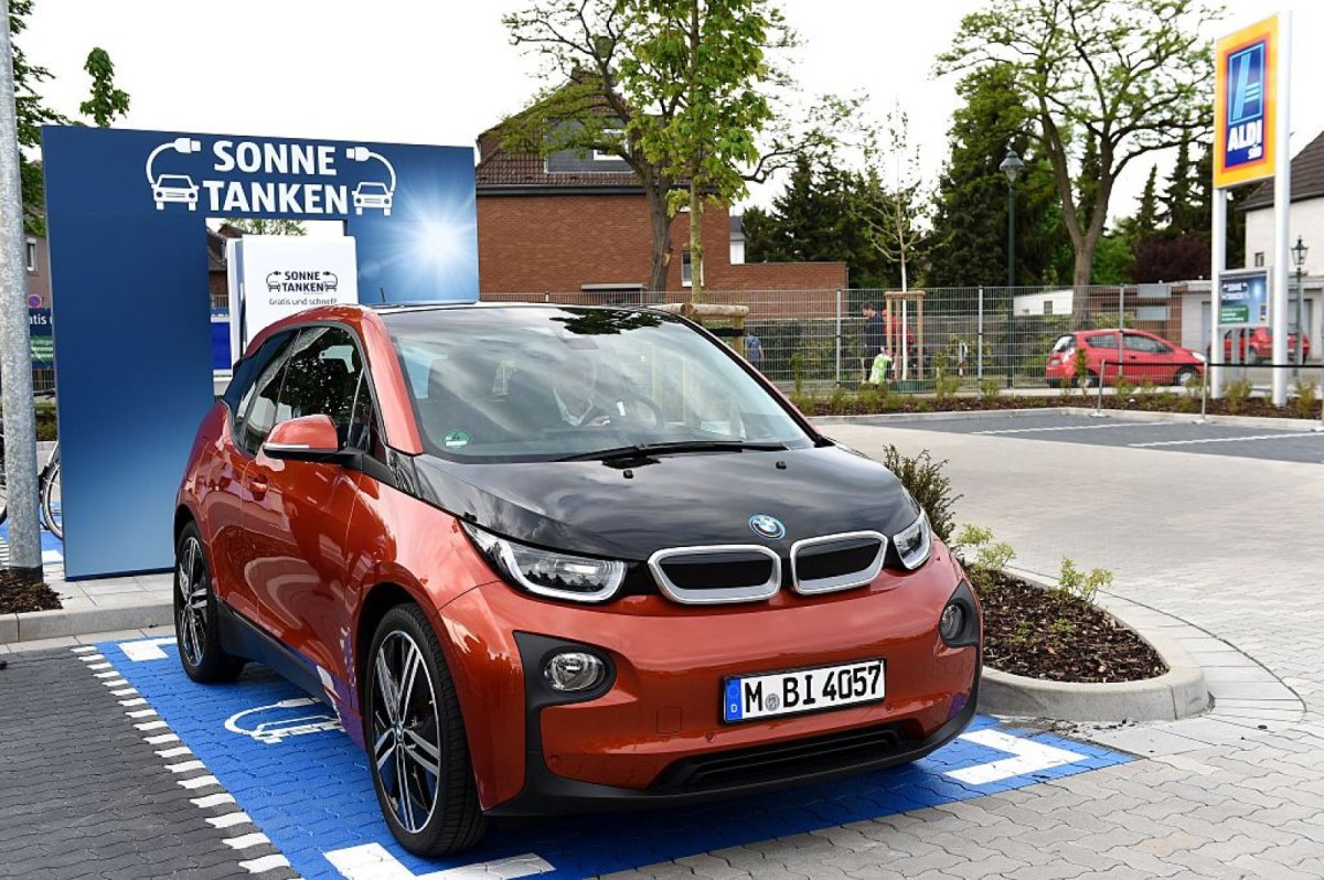 Ein Elektroauto von BMW steht vor einer Werbewand mit der Aufschrift "Sonne tanken".