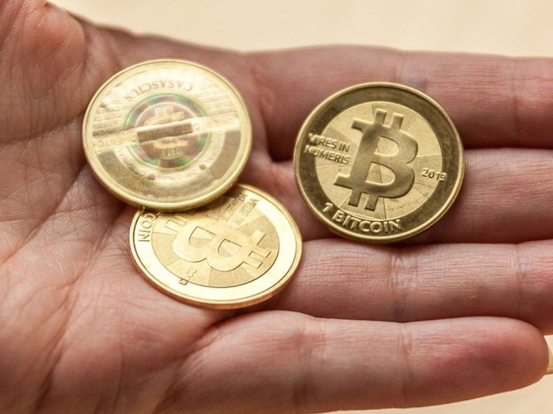 Eine Hand mit drei Bitcoin-Münzen