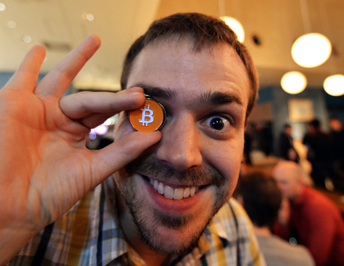 Mann hält sich Bitcoin-Münze vor ein Auge