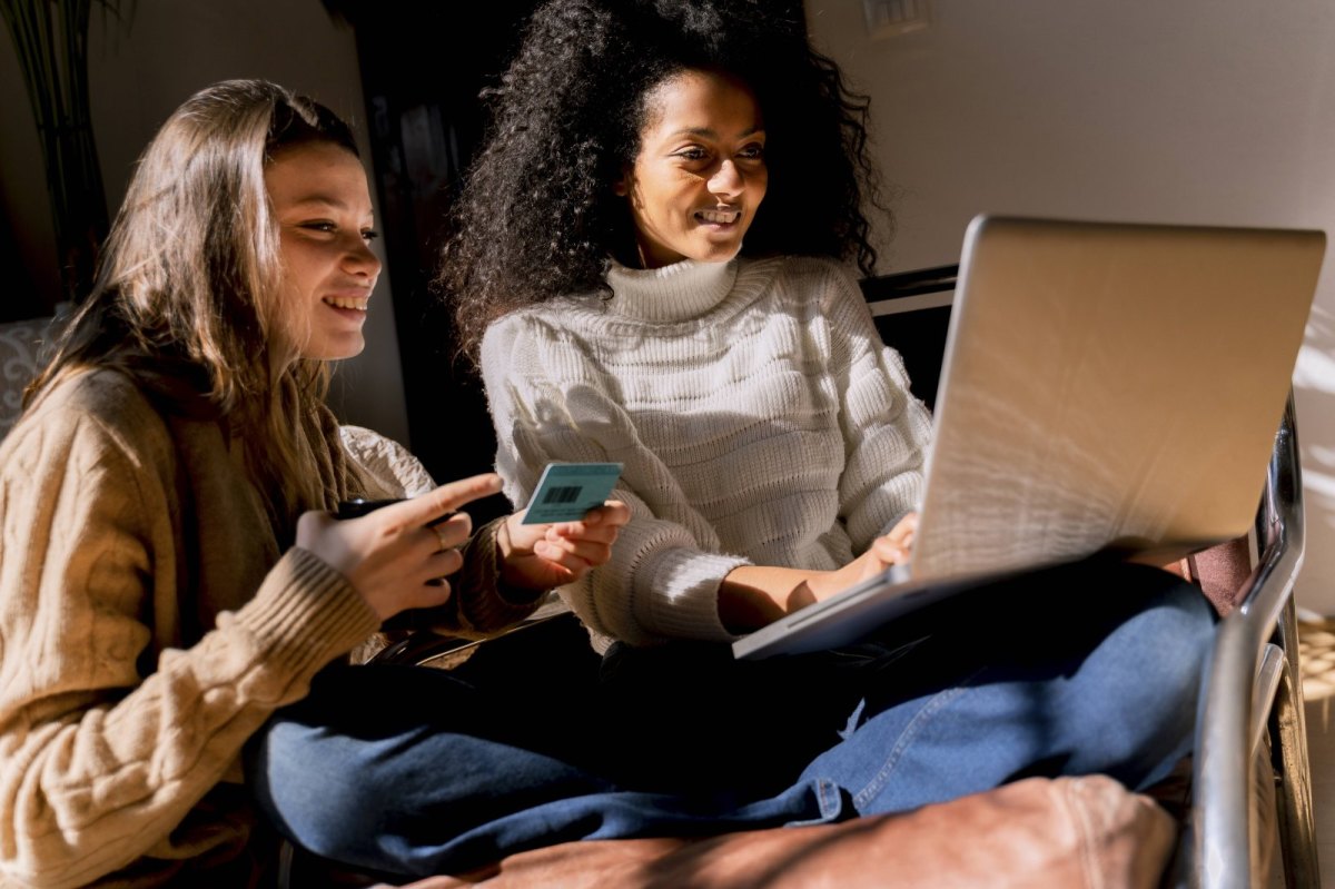 Zwei Frauen sitzen mit Laptop und Kreditkarte da.