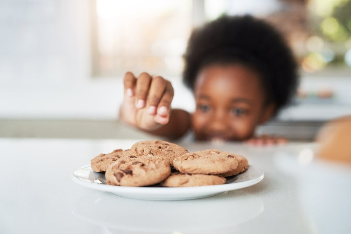 Kind stibitzt sich einen Cookie vom Teller.