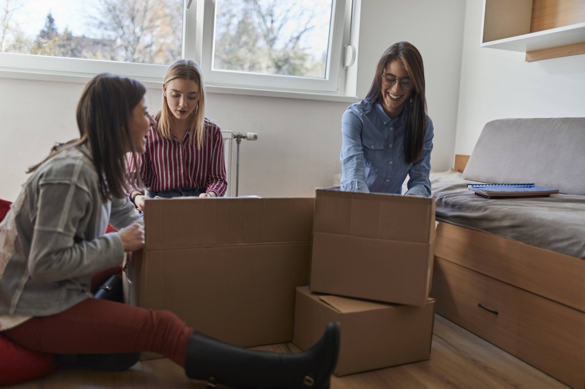 Drei junge Frauen packen Umzugskartons.