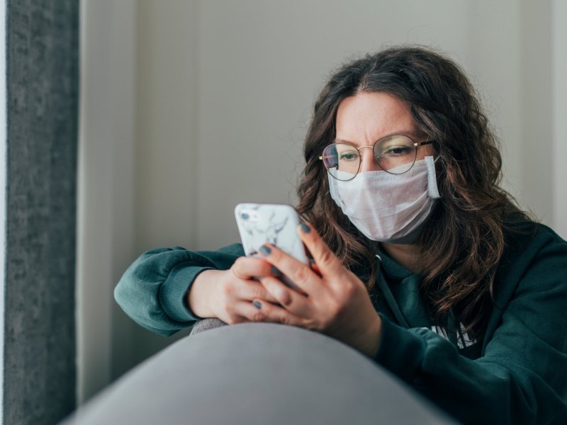 Frau mit Maske guckt auf ihr Handy.