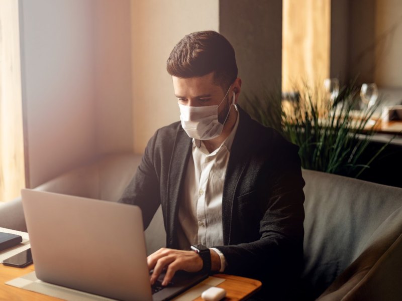 Mann sitzt mit Mundschutz vor einem Laptop.