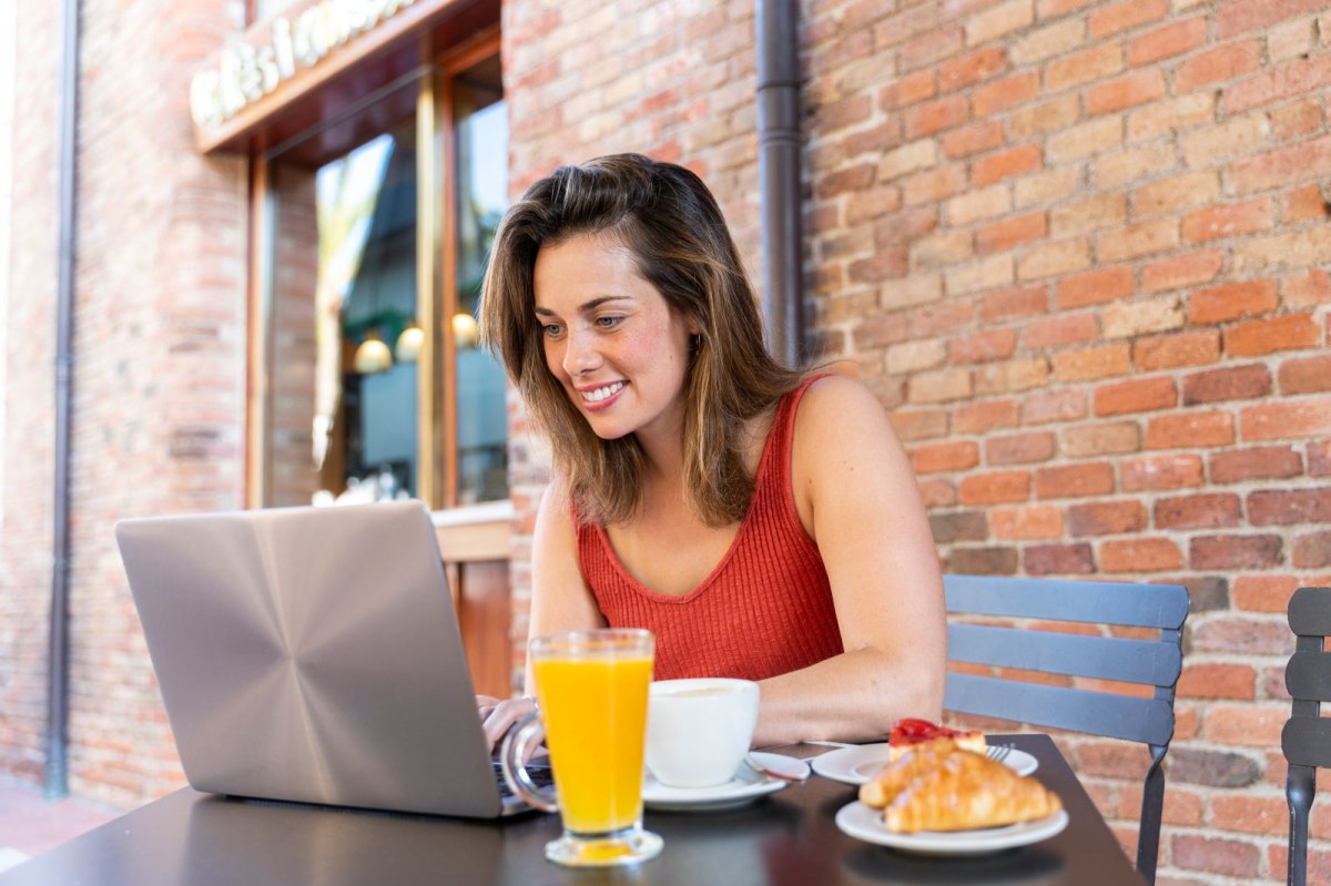 Frau sitzt lächelnd vor einem Laptop.