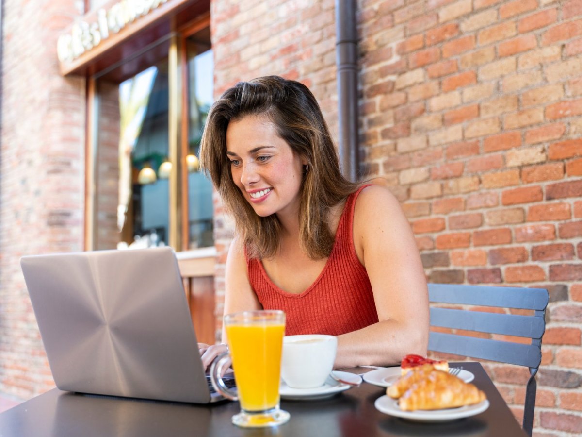 Frau sitzt lächelnd vor einem Laptop.