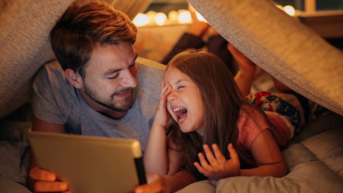 Vater und Kind liegen im Bett und schauen auf ein Tablet.