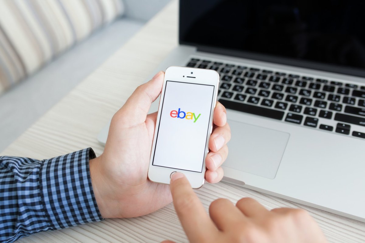 Mensch hält Handy mit eBay-Logo in der Hand.