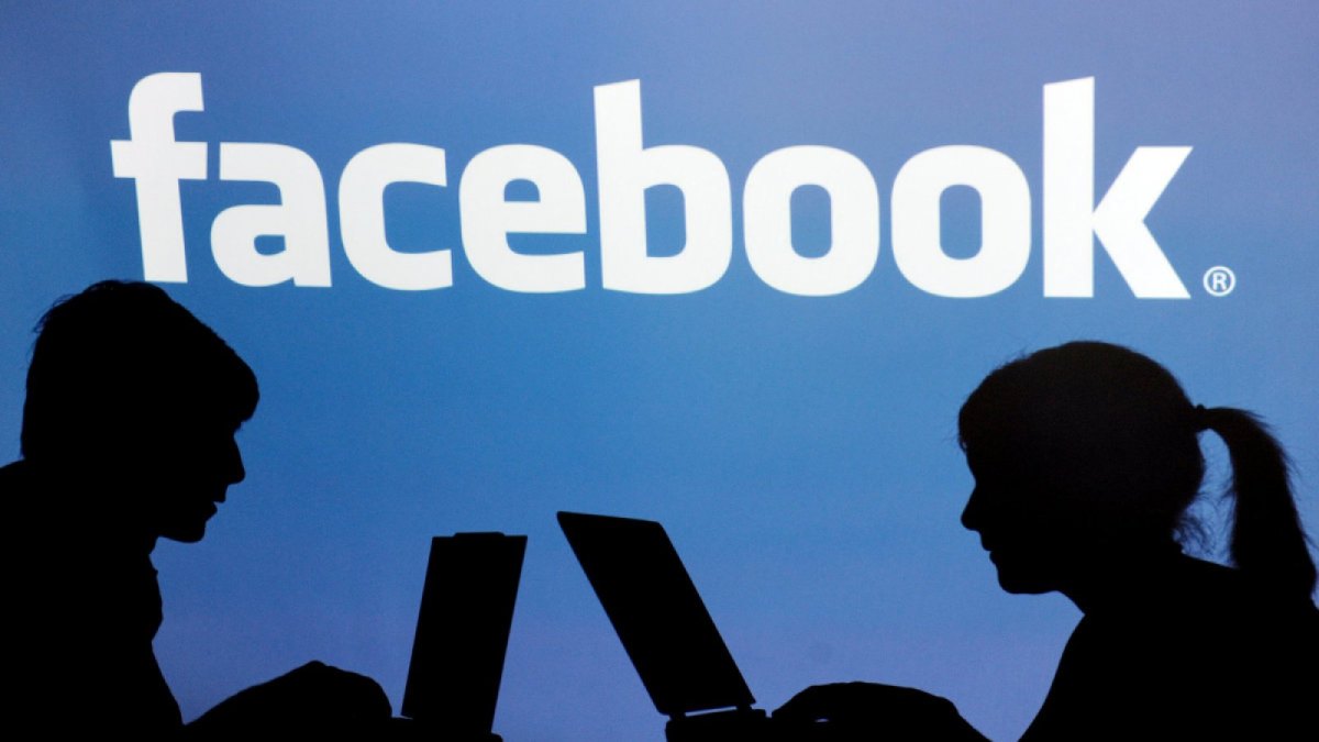 Die Silhouetten zweier Personen am Laptop vor dem Facebook-Schriftzug