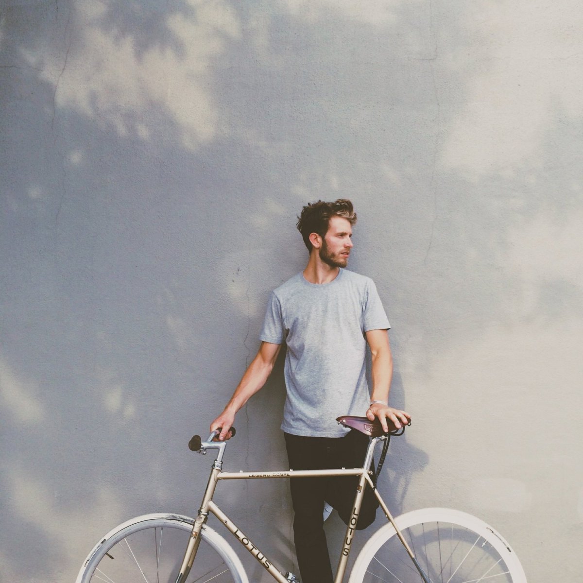 Mann lehnt an einer Wand und hat ein Fahrrad vor sich stehen.