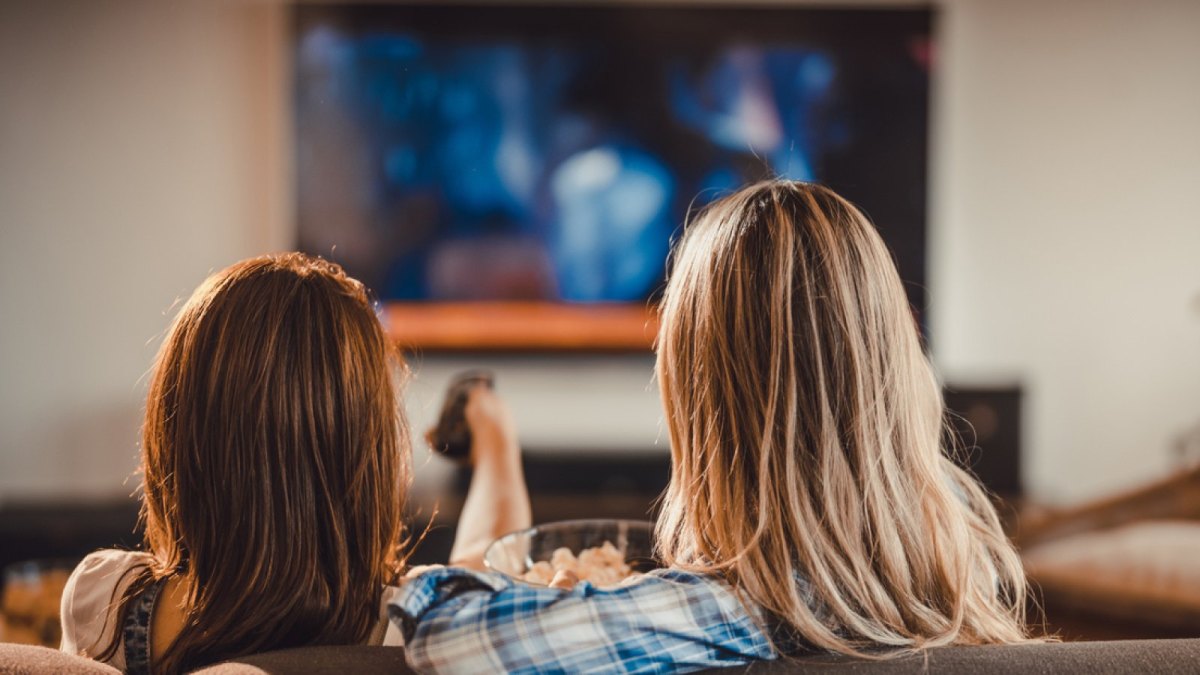 Zwei Personen sitzen auf dem Sofa vor einem Fernseher.