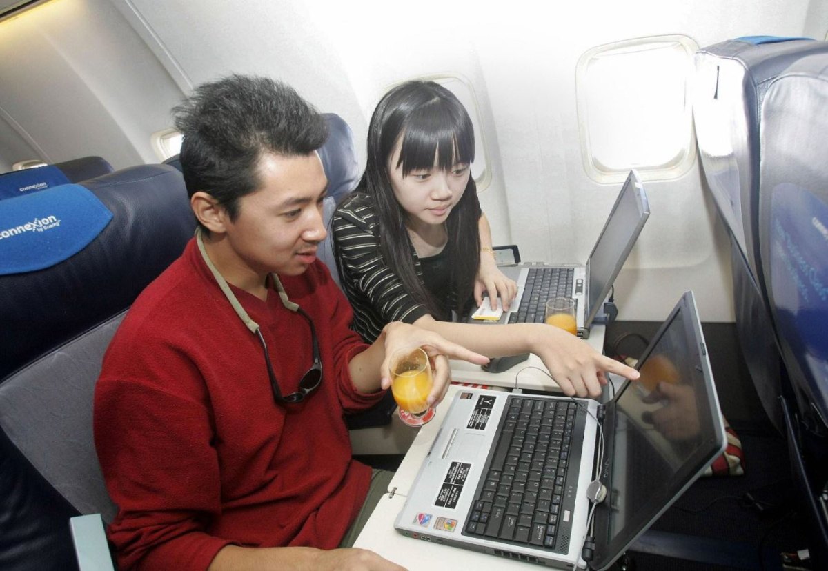 Zwei Menschen im Flugzeug schauen auf ihre Laptops und trinken Orangensaft