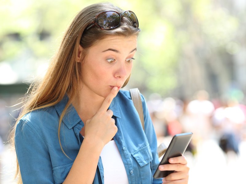 Eine Frau blickt peinlich berührt und schockiert auf ihr Handy.
