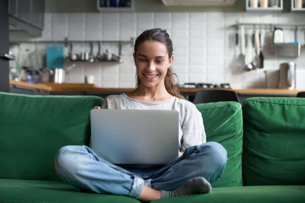 Frau sitzt auf einem grünen Sofa und hat einen Laptop auf dem Schoß.