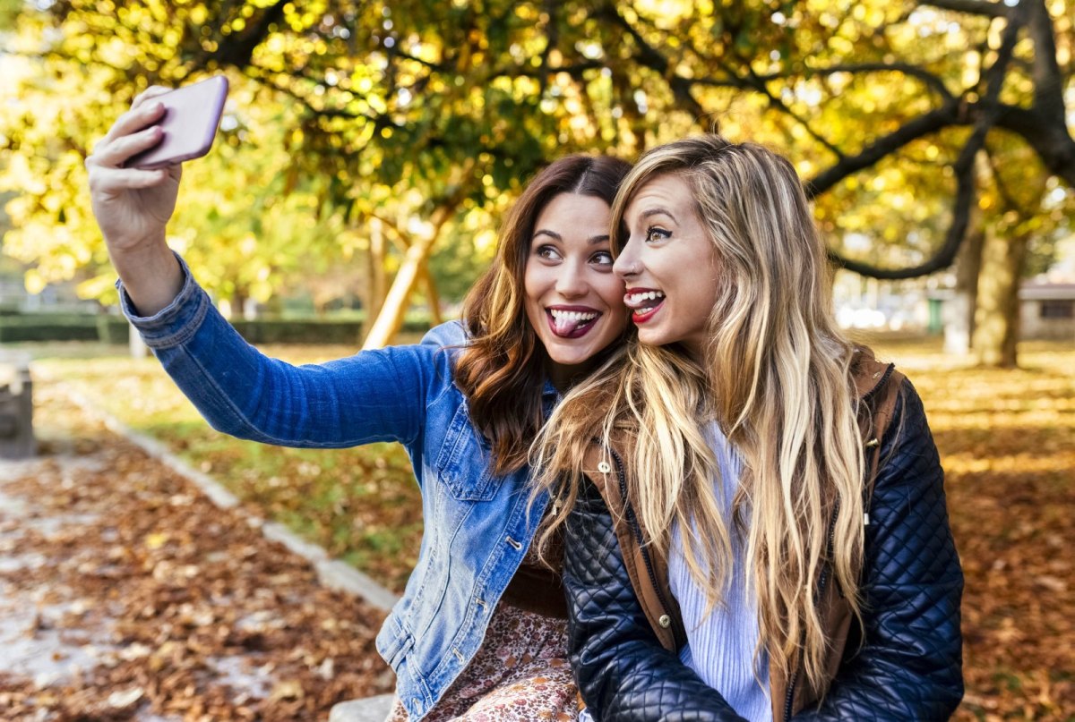 Frauen machen in einer herbstlichen Landschaft ein Selfie mit einem Smartphone.