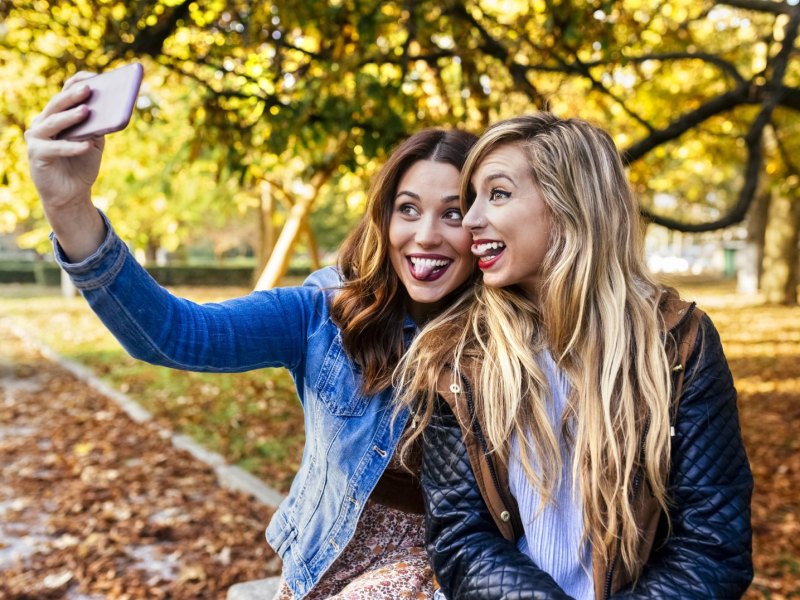 Frauen machen in einer herbstlichen Landschaft ein Selfie mit einem Smartphone.