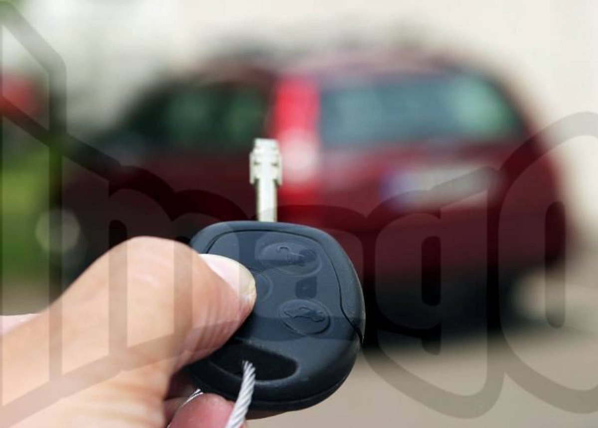 Eine Hand hält einige Meter von einem Auto entfernt den dazugehörigen Funkschlüssel.