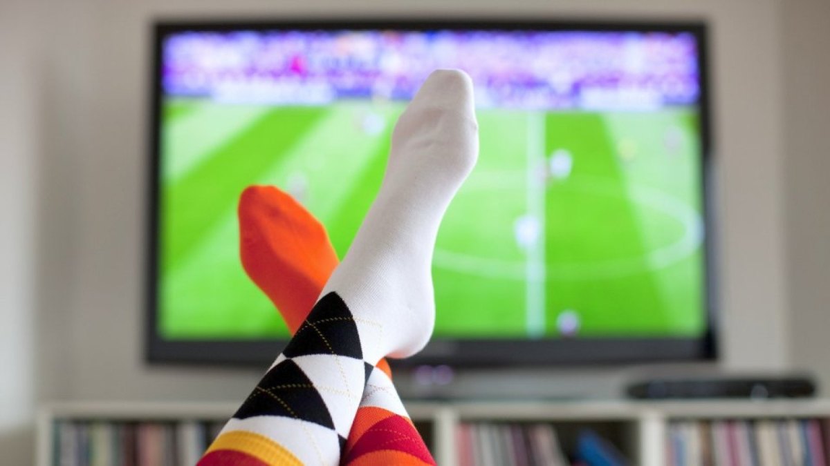 Füße mit Fußballsocken vor einem Fernseher im Hintergrund