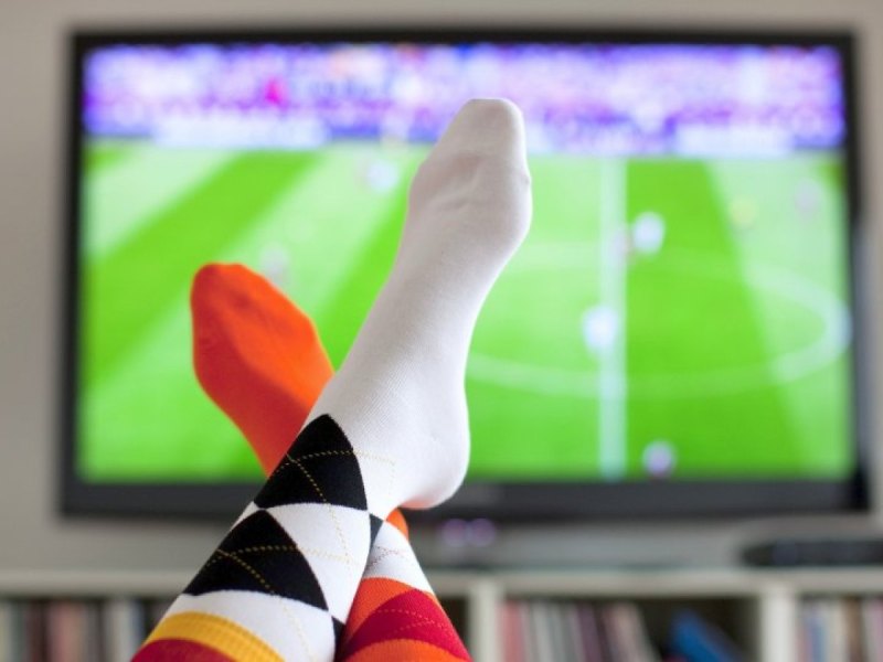 Füße mit Fußballsocken vor einem Fernseher im Hintergrund