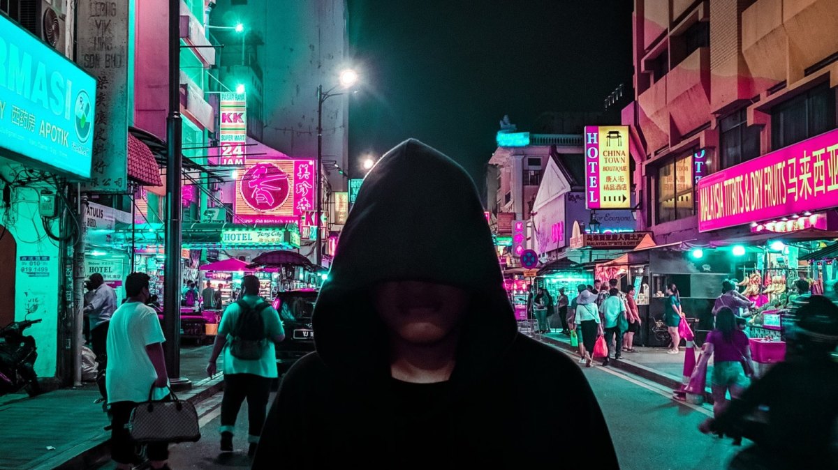 Mann mit Kapuze und verdecktem Gesicht steht auf einer beleuchteten Straße.
