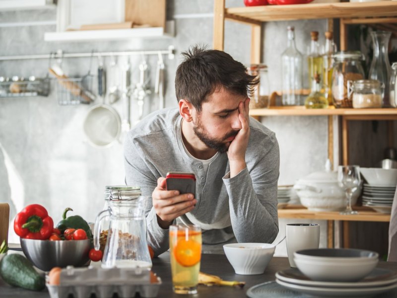 Mann in der Küche genervt mit Smartphone.