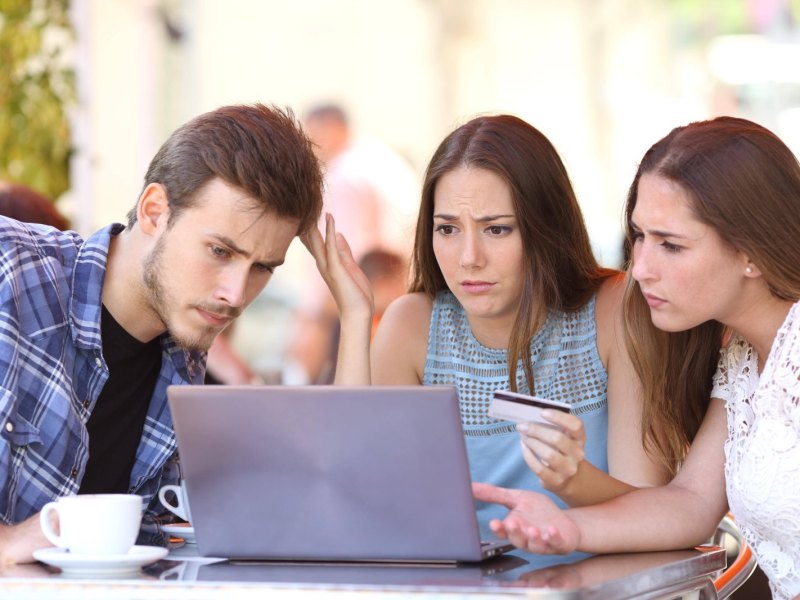 Drei junge Menschen sitzen vor einem Laptop und sind verwundert über ein Online-Shopping-Erlebnis.