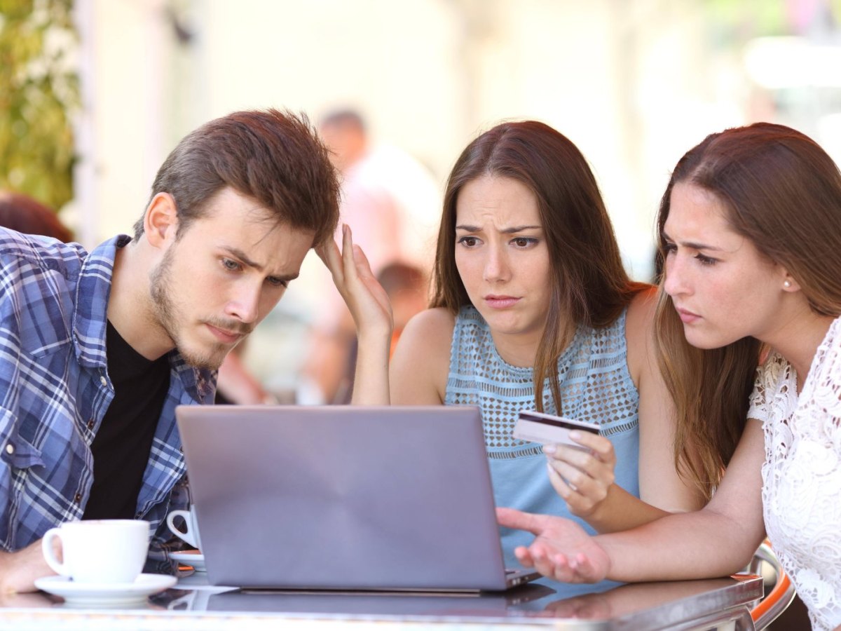 Drei junge Menschen sitzen vor einem Laptop und sind verwundert über ein Online-Shopping-Erlebnis.