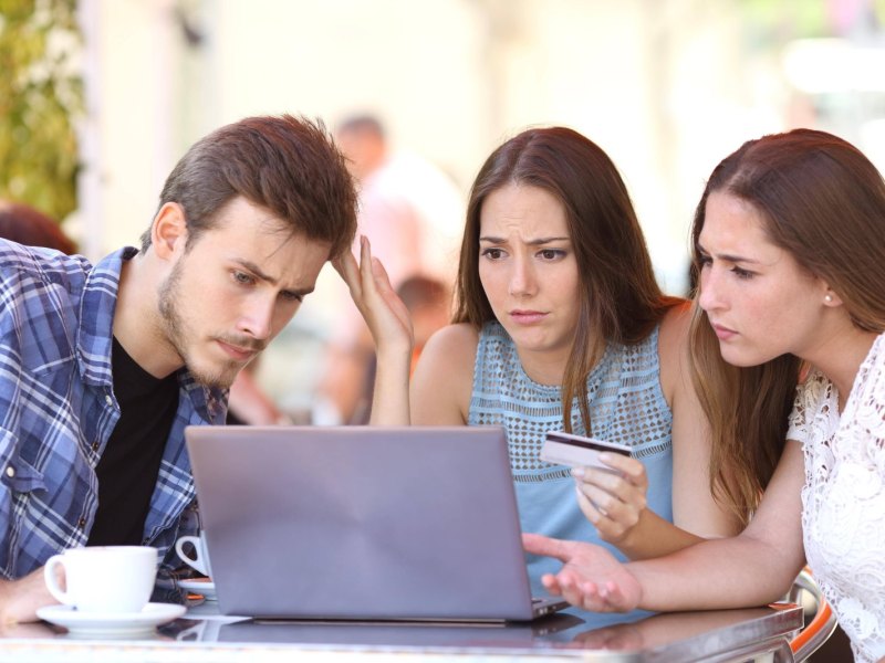 Drei junge Menschen sitzen vor einem Laptop und sind verwundert über ein Online-Shopping-Erlebnis.