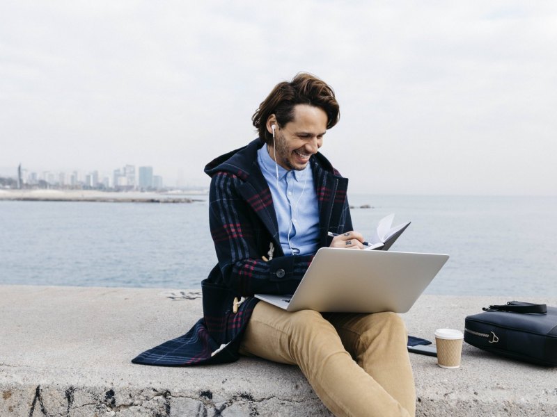 Lachender Mann beugt sich über seinen Laptop und Kalender.