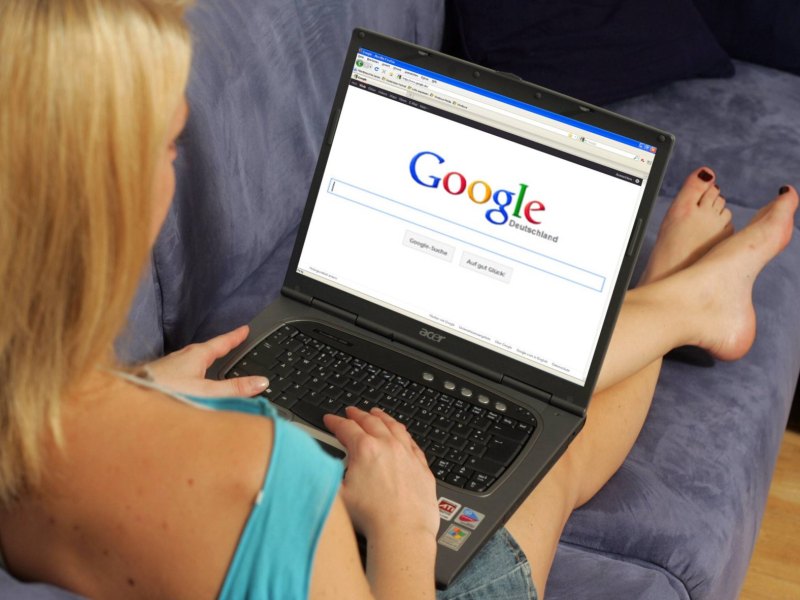 Eine Frau sitzt auf dem Sofa und googelt etwas auf ihrem Laptop.