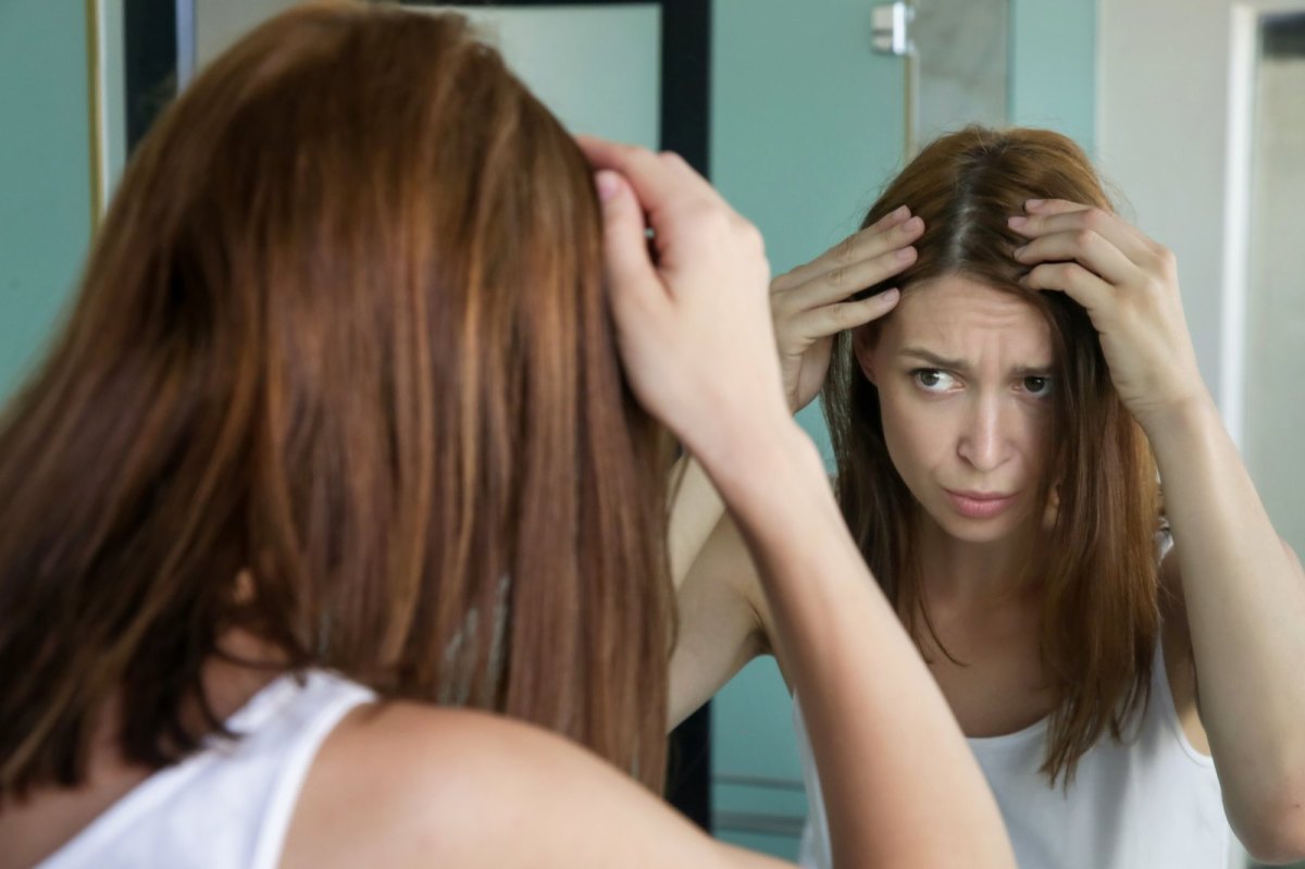 Junge Frau steht vor dem Spiegel und sieht graue Haare.
