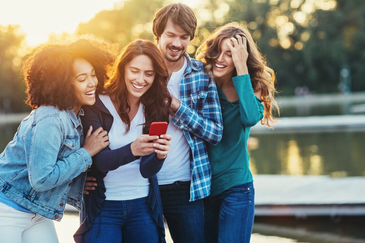 Eine Gruppe Menschen schaut lachend auf ein Smartphone.